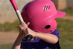 Little girl holding a pink softball bat and wearing a pink helmet that is much too big for her.